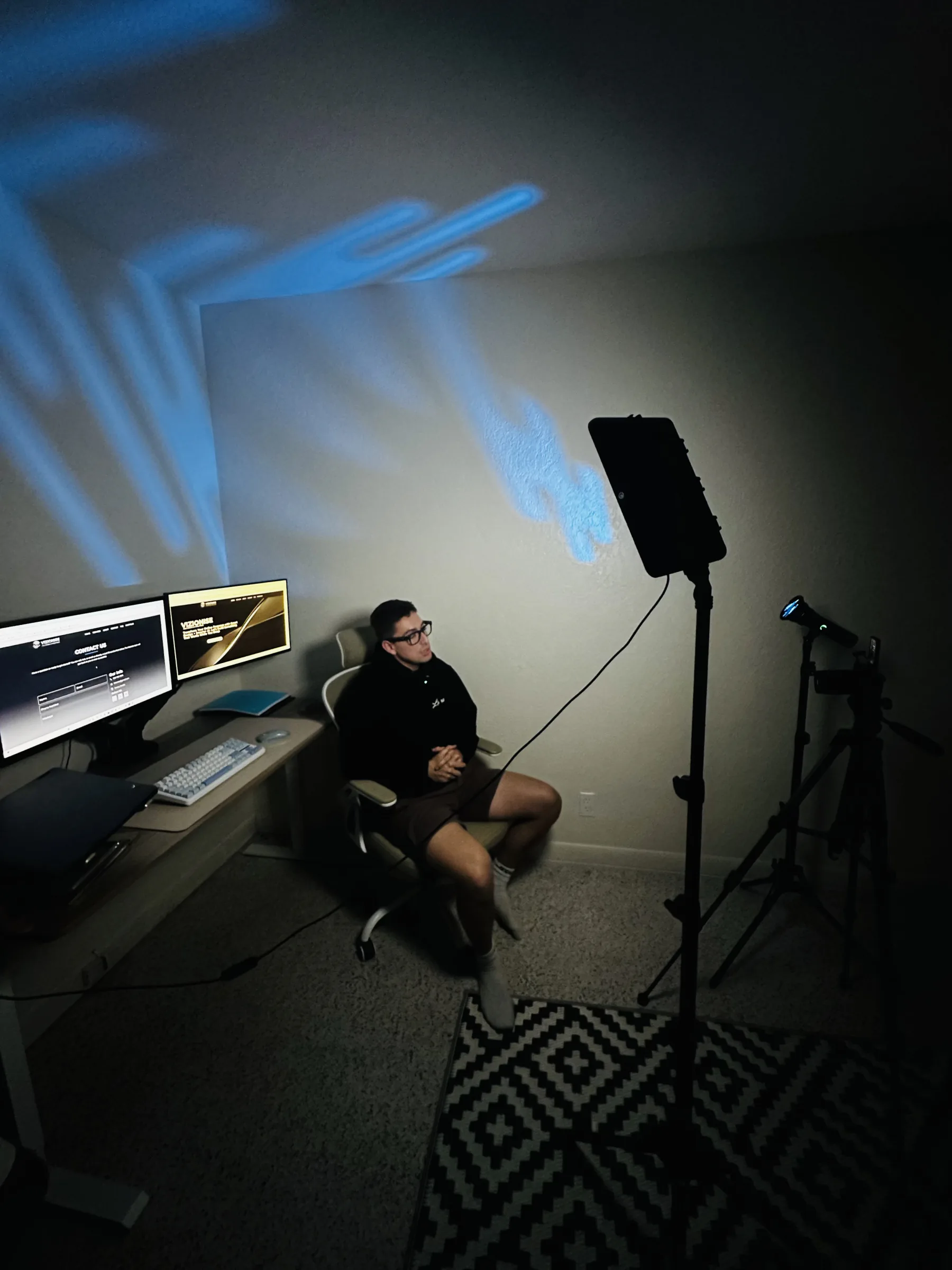 Nicholas Grande seated in his studio beside a camera and production lights